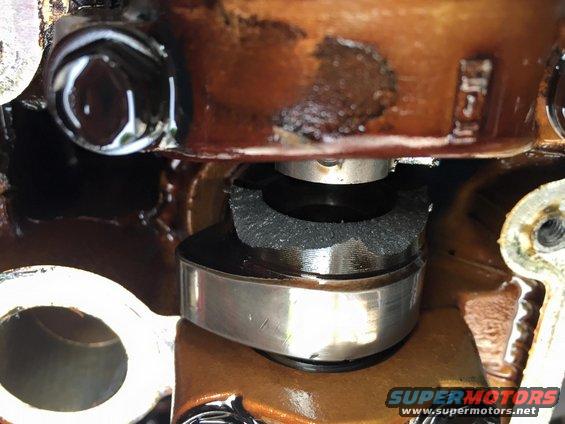 Close-up of engine valve train component with oil residue. Supermotors.net logo visible