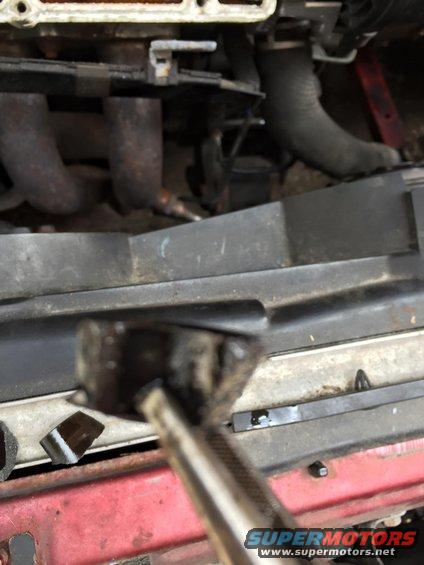 Close-up of car engine bay, showing exhaust manifold and hoses. A tool is in the foreground
