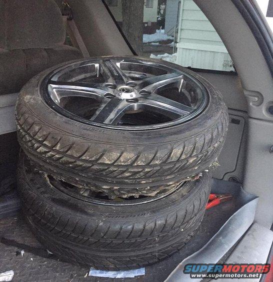 Two used tires stacked on aftermarket rims inside a vehicle's cargo area