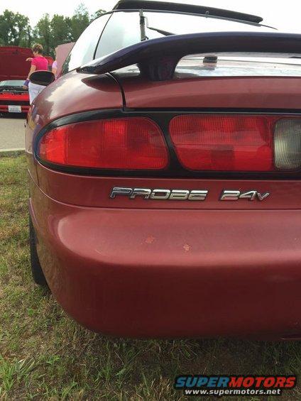 Red car rear with spoiler and 'PROBE 24V' badge. Another red car is visible in the background