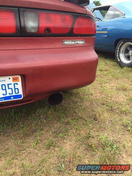 Red car rear with Mazdaspeed badge and exhaust pipe. Blue car in background