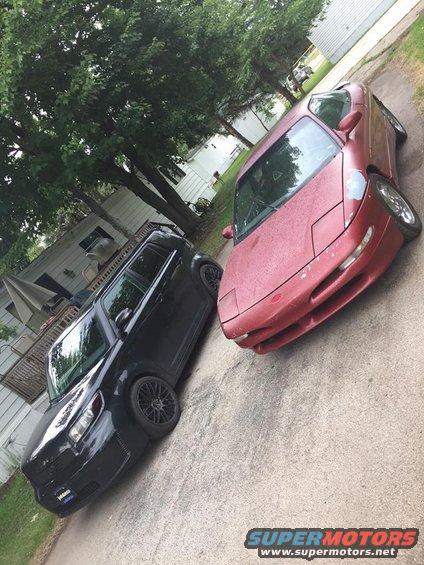 red sports car with pop-up headlights next to black SUV