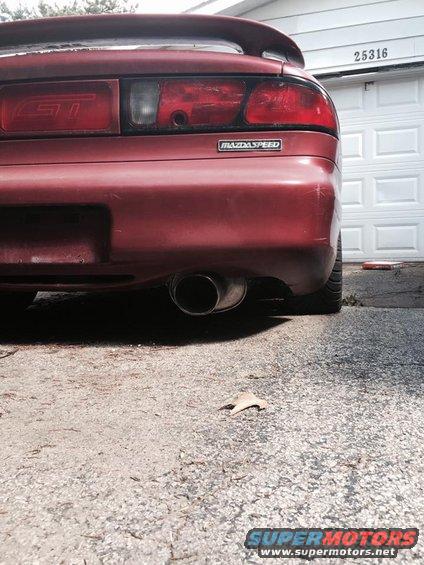 Red car's rear bumper with 'Mazdaspeed' badge and 'GT' taillight. Exhaust pipe visible