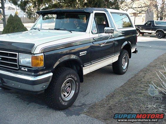 Two-tone Ford Bronco parked on a street, another Bronco in the background