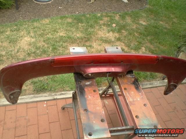 red rear spoiler with brake light mounted on sawhorses outside
