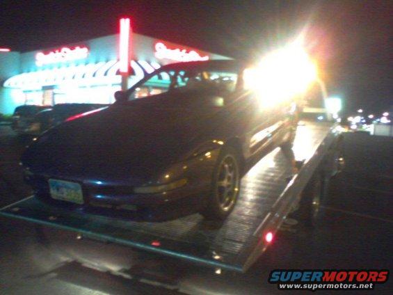 Dark coupe on a tow truck at night, front quarter view. License plate visible
