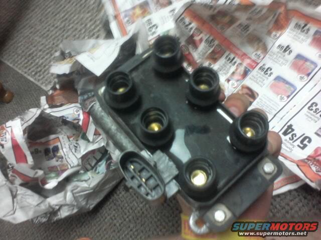 Ignition coil pack with five spark plug wires and a connector, held by a hand over crumpled newspaper