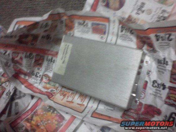 Rectangular metal electronic component with a label on it, resting on a spread of newspapers