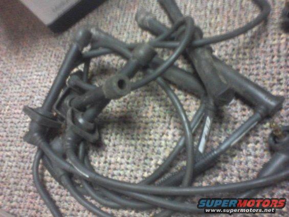 Bunch of black spark plug wires tangled up on a carpeted surface