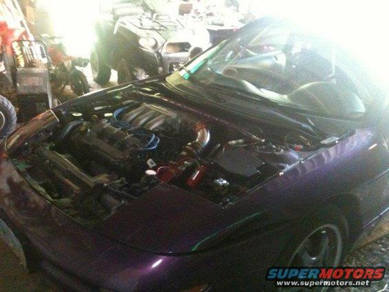Purple car with hood open, showing engine bay. Visible in background are an ATV and motorcycle