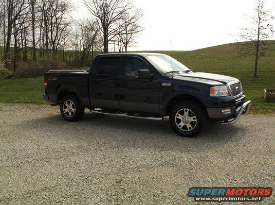 Dark blue Ford F-150 pickup truck, front quarter view, parked on gravel. Chrome bull bar on front bumper