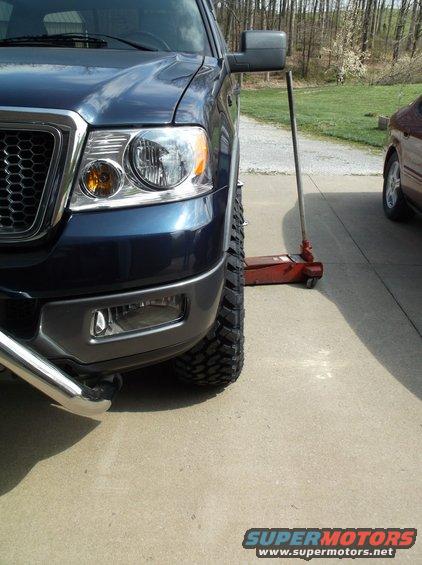 Front wheel and fender of a blue 2005 Ford F-150, jacked up