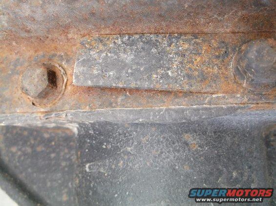 Close-up of rusted metal frame with a bolt and part of a black component