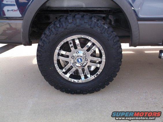 Chrome alloy wheel with off-road tire on a dark-colored vehicle, close-up side view