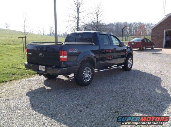 Dark blue Ford F-150 pickup truck with FX4 Off Road badging, parked on gravel. Red sedan in background