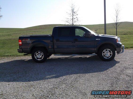 Dark blue Ford F-150 pickup truck, side view, aftermarket wheels, chrome side steps, tonneau cover