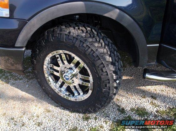 Truck's front wheel with chrome rim and off-road tire, showing fender and side panel