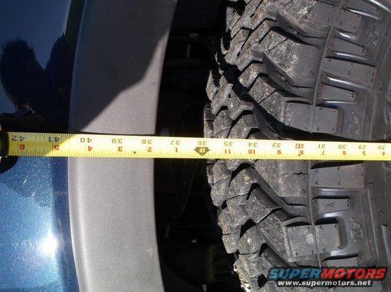 Measuring tire diameter against vehicle fender with a yellow tape measure