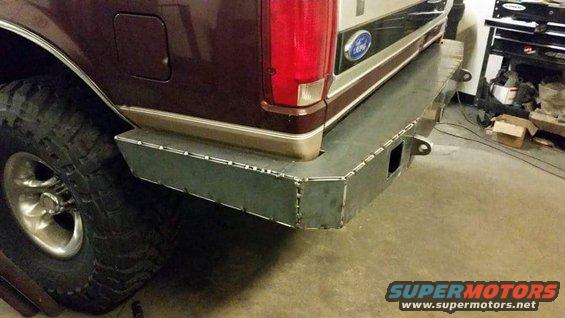 Maroon Ford Bronco with custom metal rear bumper and large off-road tire. Visible Ford logo on tailgate