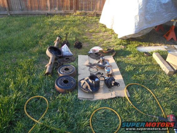Vehicle axle housing, differential gears, brake drums, and other parts laid out on grass