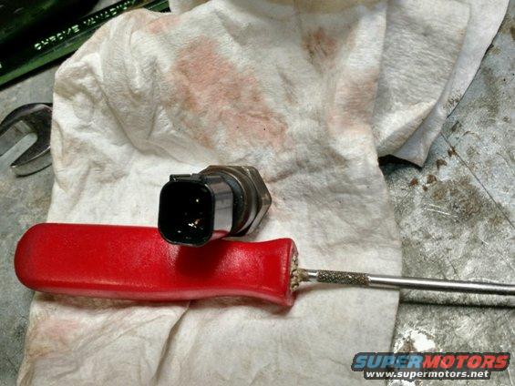 Power steering pressure sensor with black connector resting on a red-handled screwdriver, on a stained white cloth