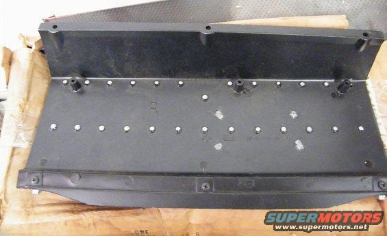 Black plastic automotive part with numerous small holes and mounting posts. Text "SUPERMOTORS.NET" visible at bottom right