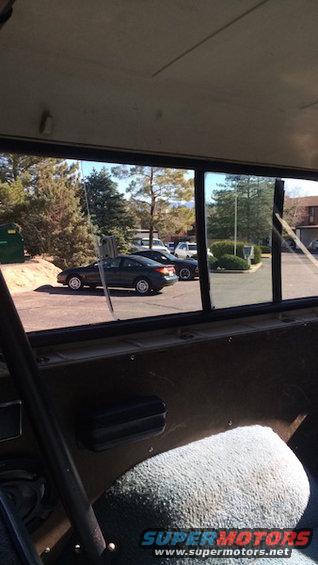 Interior view of a 1980 Ford Bronco looking out at a parking lot with a dark sedan and a white SUV