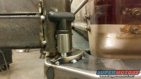 Metal latch mechanism with black handle attached to a raw metal bracket, with a brown and chrome part in the background