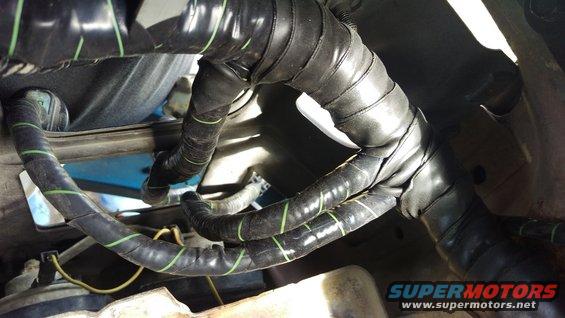 Close-up of a vehicle's engine wiring harness with black tape and green stripes