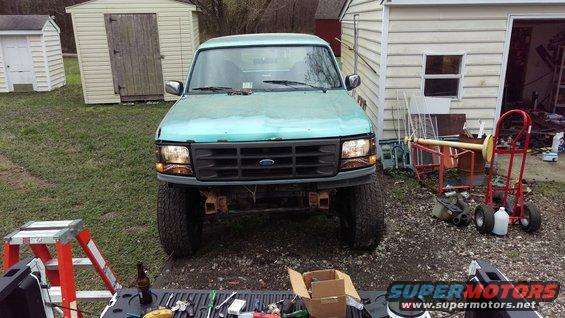 1990s Ford Bronco front view, teal paint, aftermarket bumper, parked in yard with sheds
