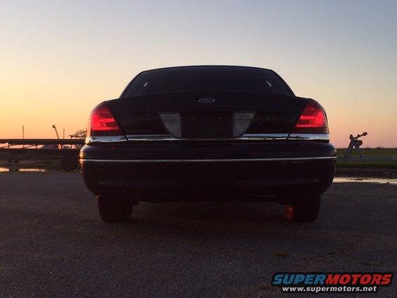 Rear view of a black Ford Crown Victoria at sunset. The taillights are illuminated