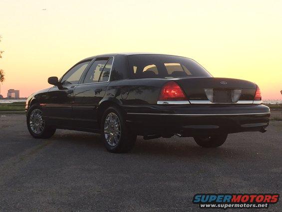 Black 2008 Ford Crown Victoria rear 3/4 view, parked on asphalt near water at sunset