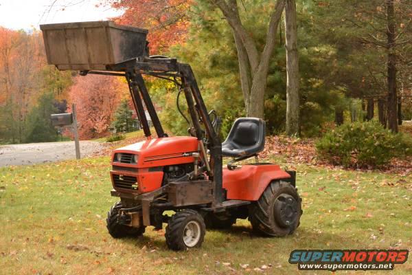 Orange tractor with front loader in a grassy yard with fall foliage
