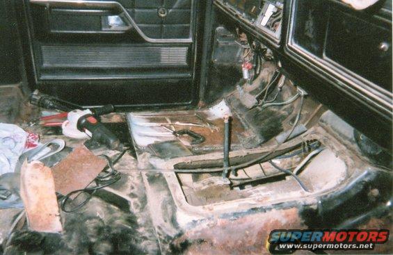 Interior of a vehicle with floor rust and tools, including an angle grinder