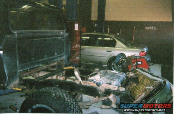 Truck chassis in foreground, silver sedan in background in garage