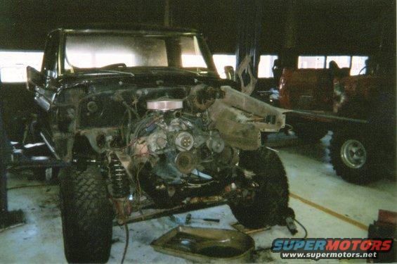 Black 1978 Ford Bronco undergoing repair, front view, engine exposed, lifted on a rack