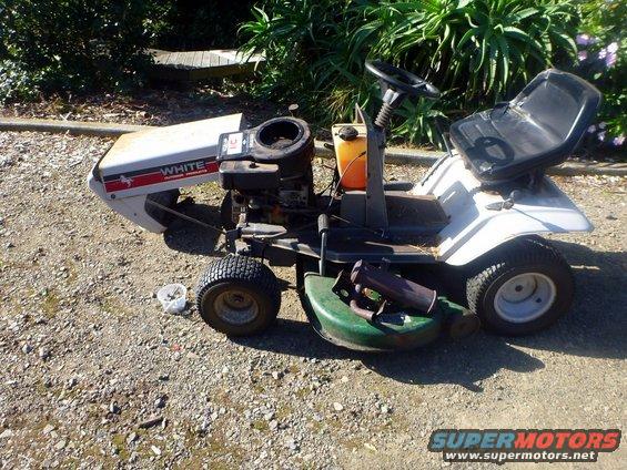 White riding lawn mower with a green deck and black seat, parked on gravel