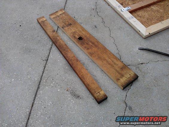 Two wooden planks lie on concrete next to a wooden frame with metal brackets. A pry bar is visible
