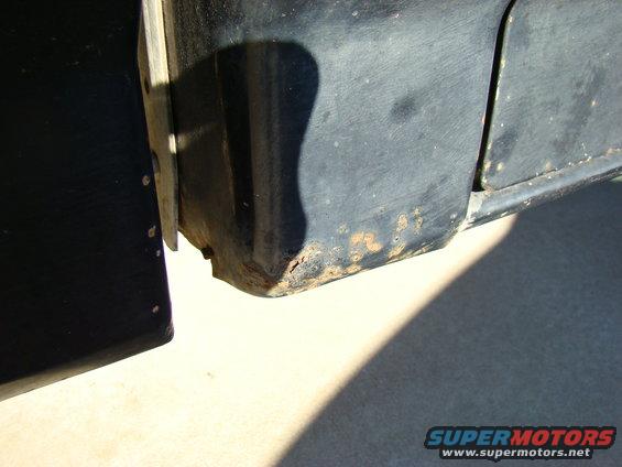 Close-up of rusted lower rear corner of a black vehicle.