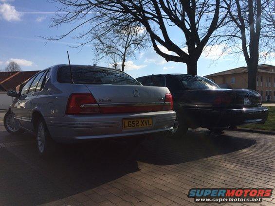 Silver sedan and black sedan parked side-by-side on a brick surface with trees overhead