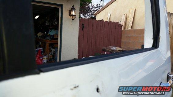 Side of white vehicle, looking past open window towards garage and fence