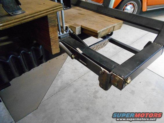 Trailer hitch mechanism with wooden platform and orange vehicle in background