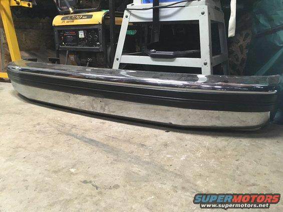 Chrome bumper with a black rubber strip, resting on a concrete floor