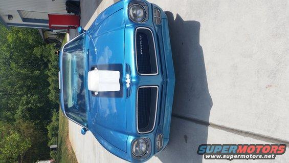 Blue Pontiac Firebird with a white hood scoop and black stripe. The grille has 'PONTIAC' written on it