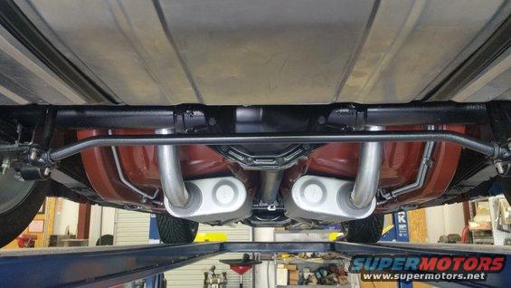 Underside of a car showing the rear suspension, fuel tank, and dual exhaust system with mufflers