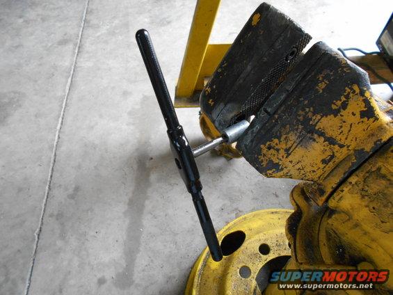 tap wrench clamped in a yellow vise, with a yellow wheel rim below