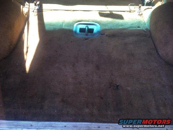Brown carpeted cargo area with a blue latch and metal trim