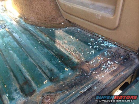 Interior floor of a vehicle with scattered broken glass and some rust damage