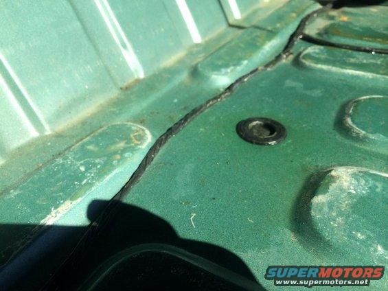 Green interior floor pan with a black rubber grommet and a seam. Supermotors.net logo visible