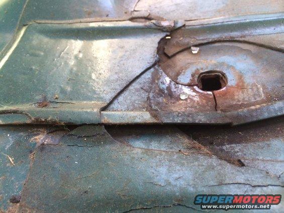 Close-up of a corroded metal panel with a square hole and some debris